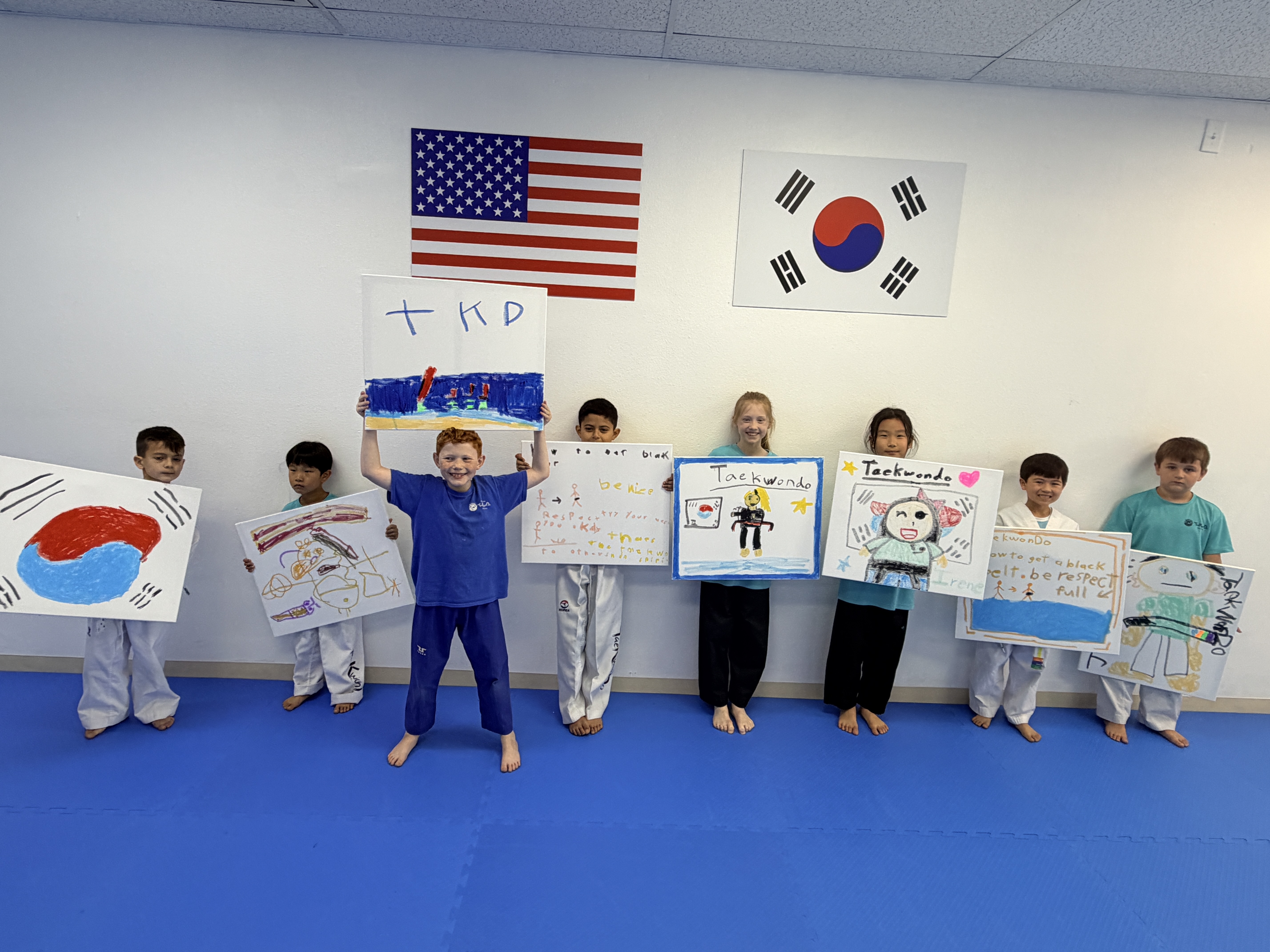 Students holding their Taekwondo paintings beneath the American and Korean flags