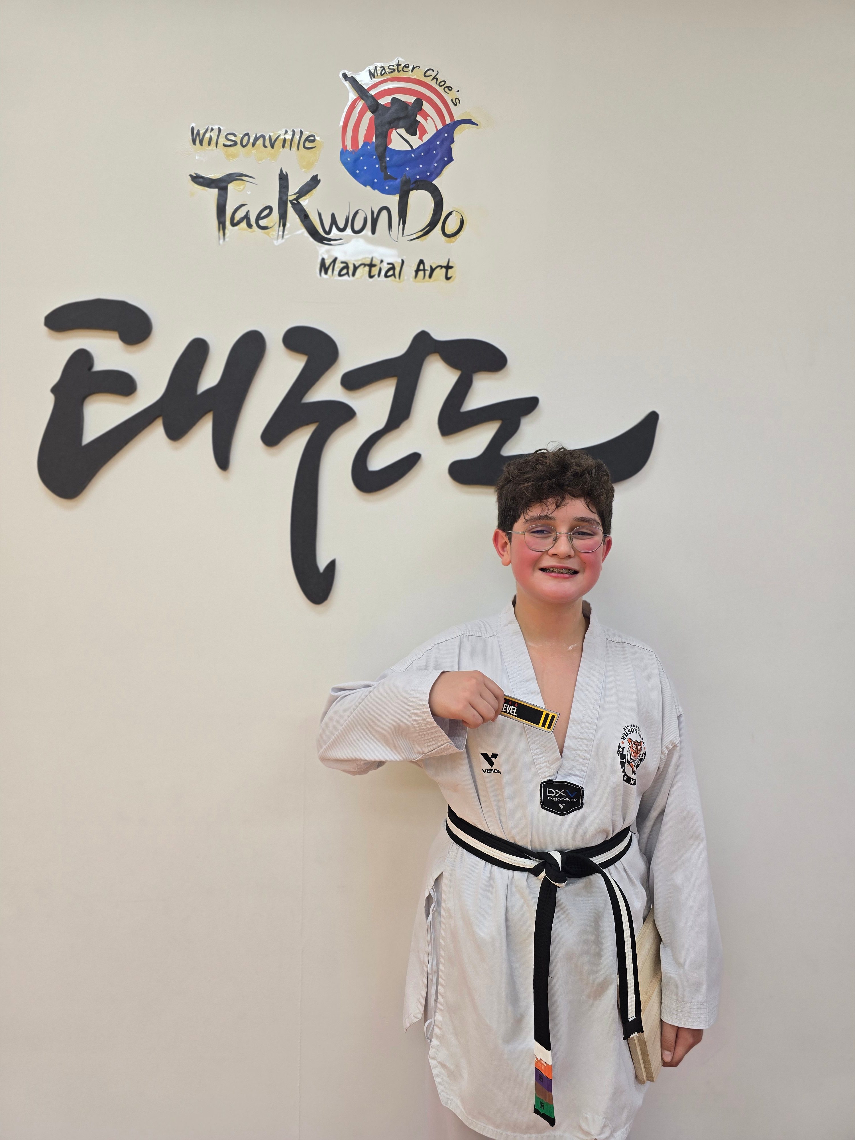 Student proudly holding his new black belt level tag in front of the academy logo