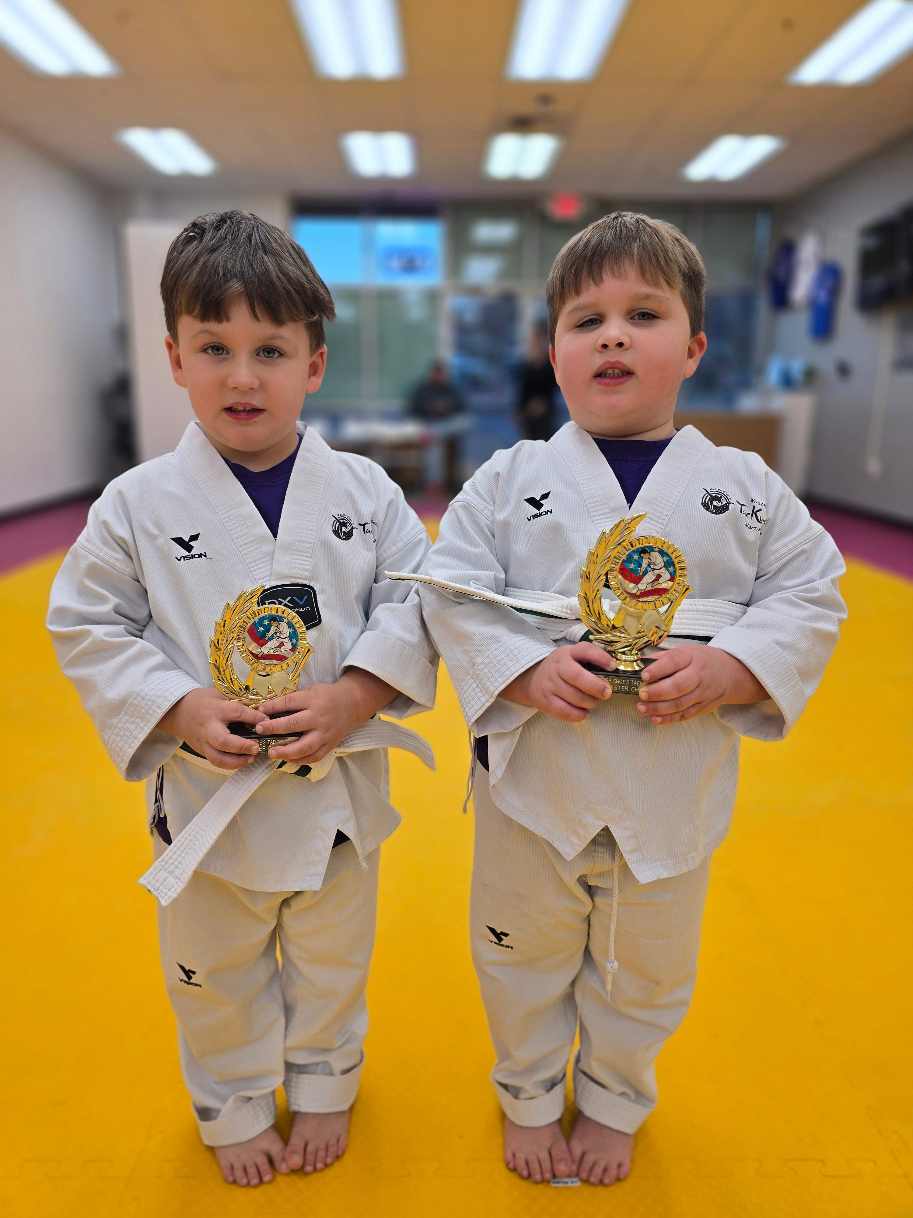 Two young white belt students holding trophies