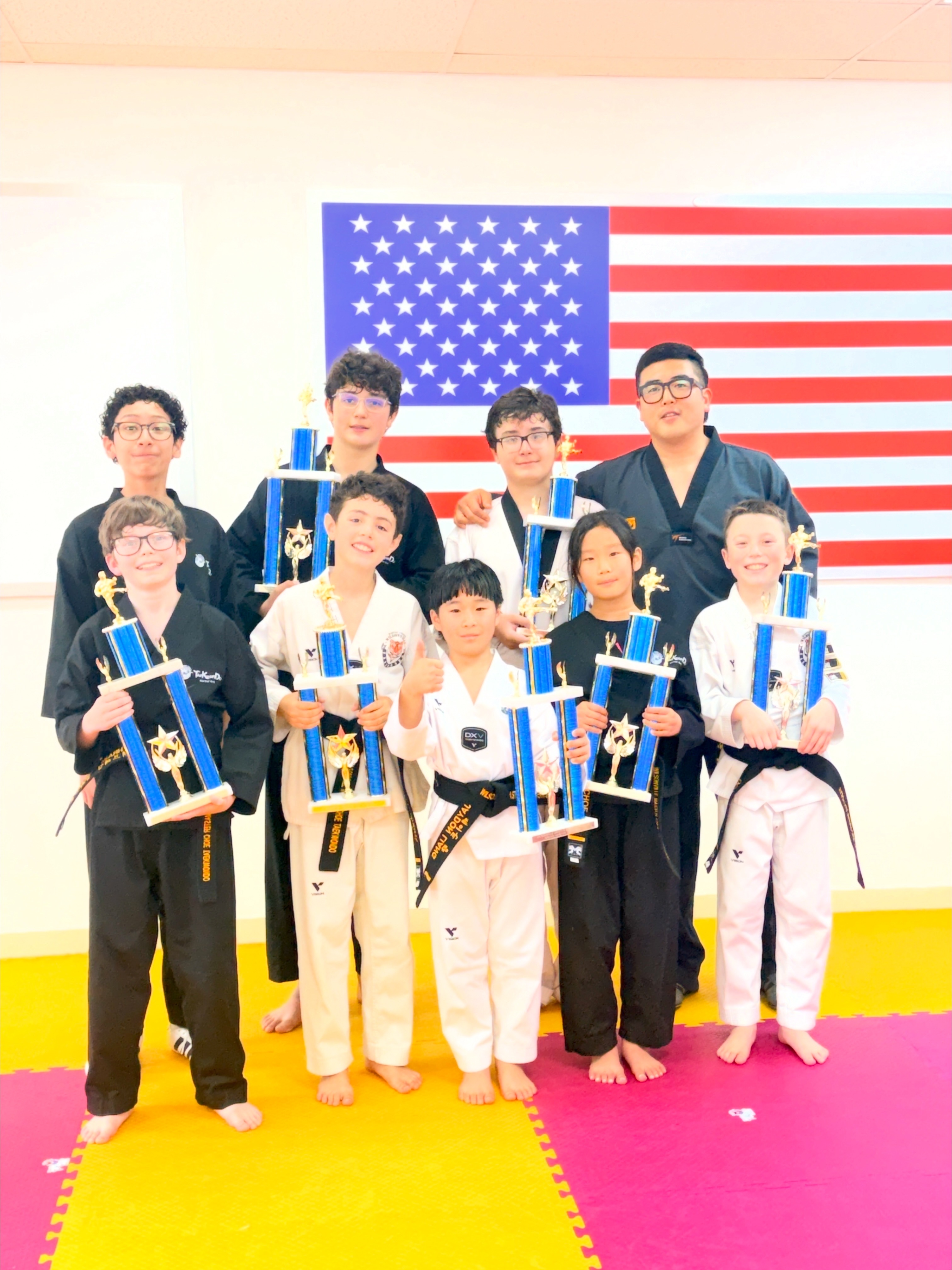 Black belt students and their instructor holding championship trophies in front of the American flag