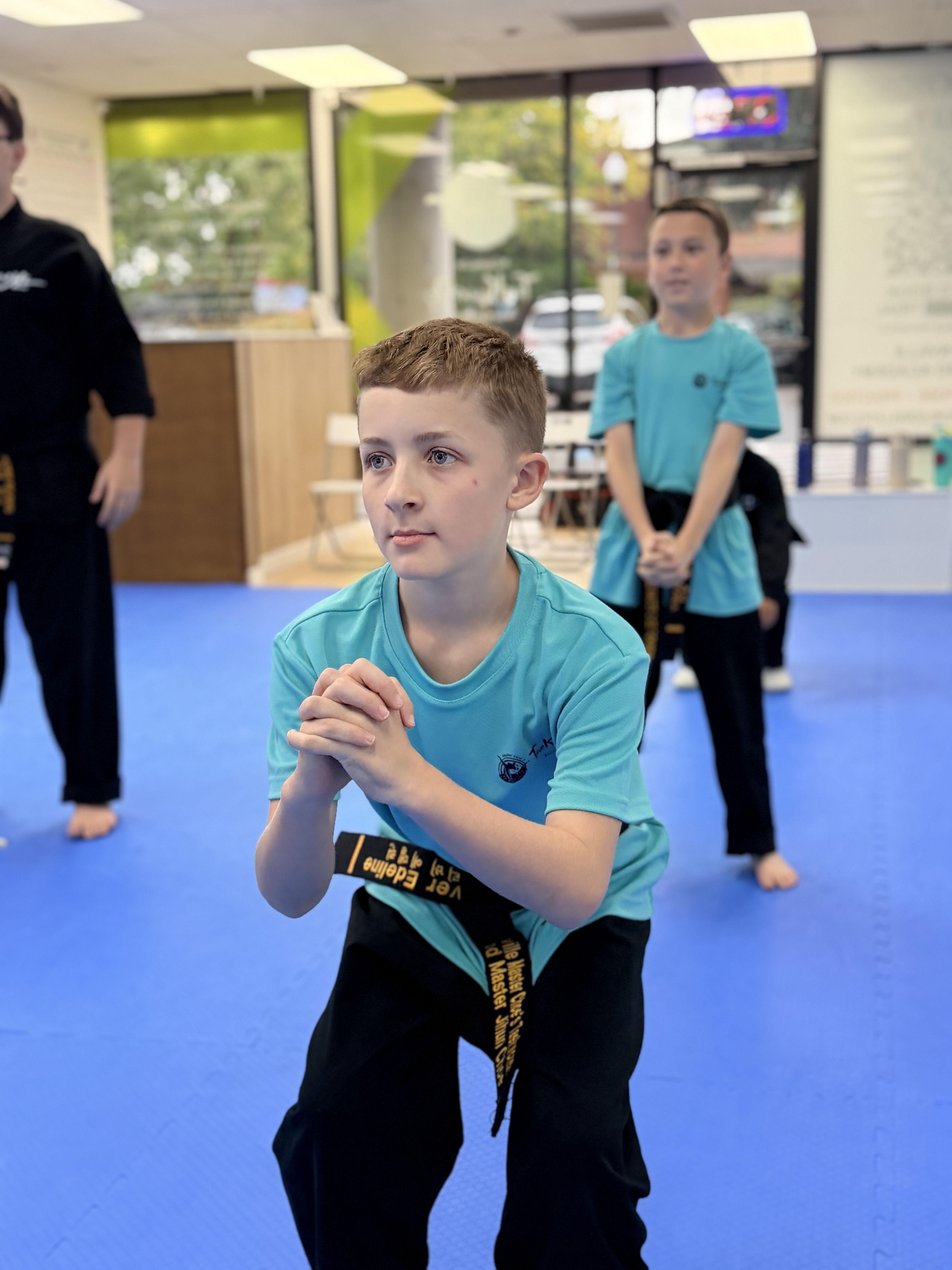 A focused black belt student in a squat stance during class
